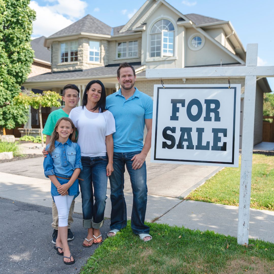 Family standing in front of house with a for sale sign Alan Fishman Coldwell Banker Realty Franklin County PA
